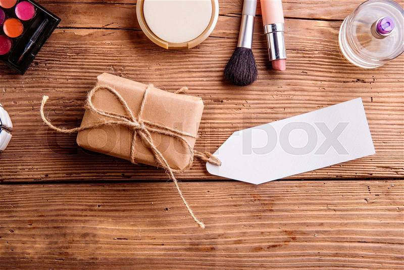 Little package with empty tag and various make up products. Studio shot on wooden background. Copy space, stock photo