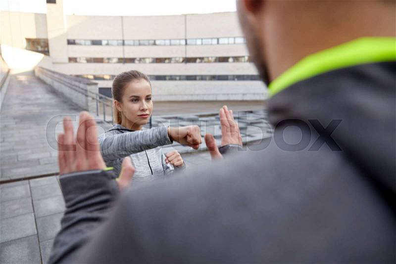 Fitness, sport, people, exercising and martial arts concept - young woman with trainer working out self defense strike on city street, stock photo