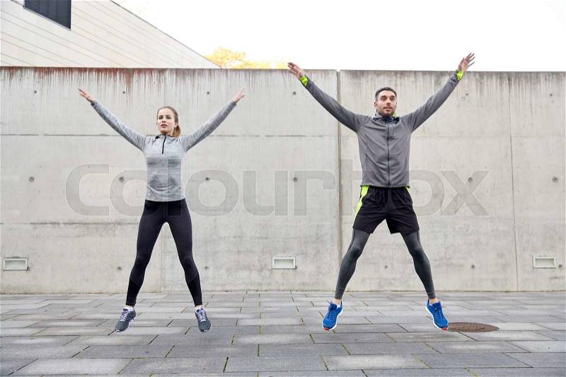Fitness, sport, people, exercising and lifestyle concept - happy man and woman doing jumping jack or star jump exercise outdoors, stock photo