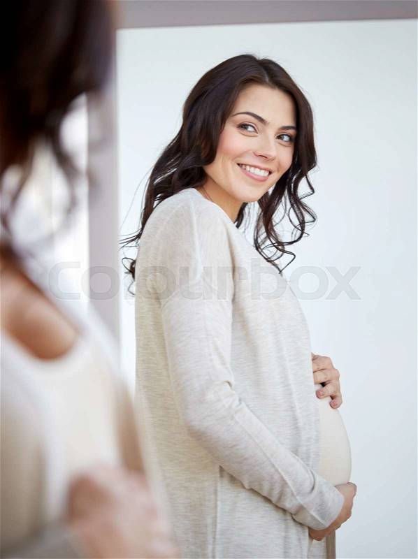 Pregnancy, motherhood, people and expectation concept - happy pregnant woman looking to mirror at home, stock photo