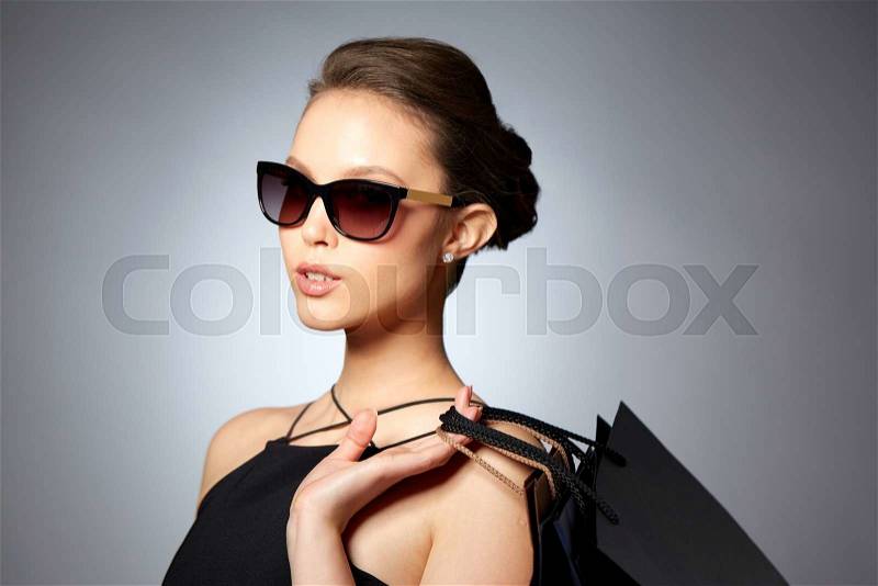 Sale, fashion, people and luxury concept - happy beautiful young woman in black sunglasses with shopping bags over gray background, stock photo