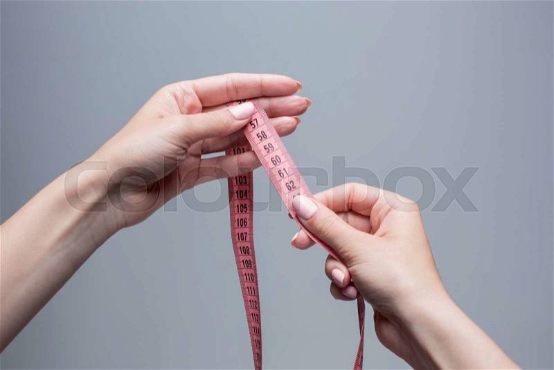 The tape in female hands on gray background. Weight loss, diet and detox concept, stock photo