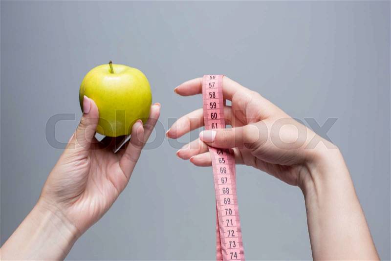 Green apple and tape in female hands on gray background. Weight loss, diet and detox concept, stock photo