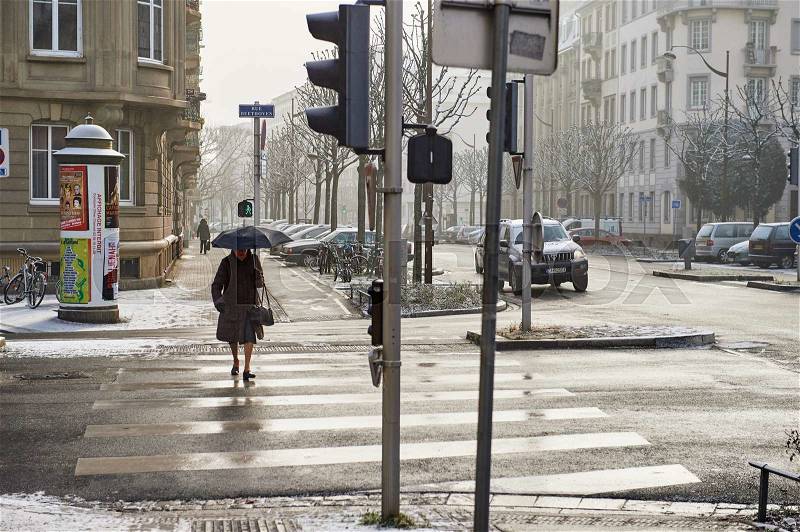 STRASBOURG, FRANCE - JAN 20, 2016: Silhouette of woman crossing street with umbrella on a snowy day, stock photo