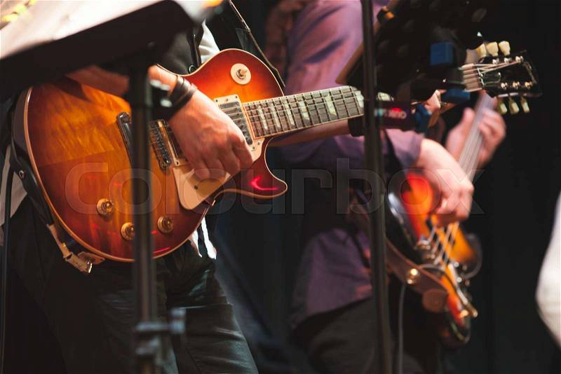 Rock and roll music background, guitar players on a stage with colorful illumination, selective focus, stock photo