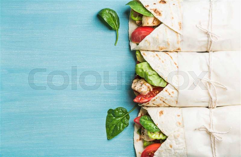 Healthy lunch snack. Tortilla wraps with grilled chicken fillet and fresh vegetables on blue painted wooden background. Top view, copy space, stock photo