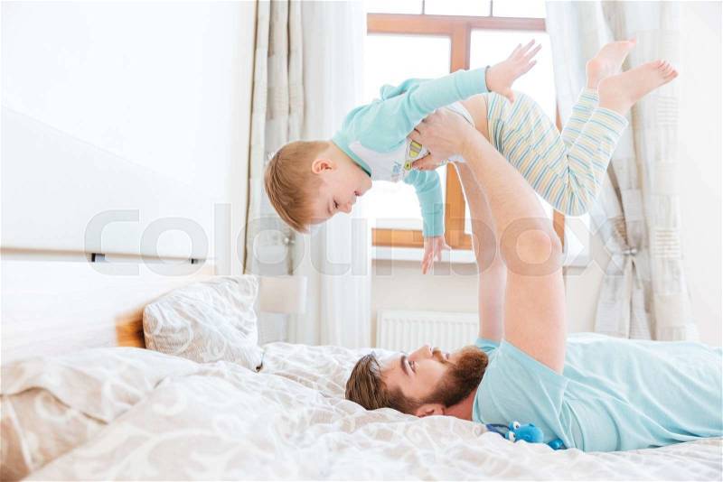 Happy handsome young father lying on bad and playing with his son , stock photo