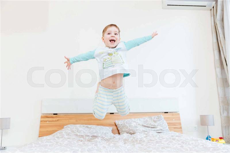 Happy little boy jumping on bed in bedroom, stock photo