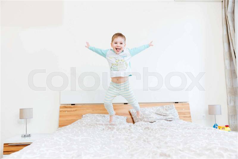 Cheerful little boy showing tongue and jumping on bed at home , stock photo