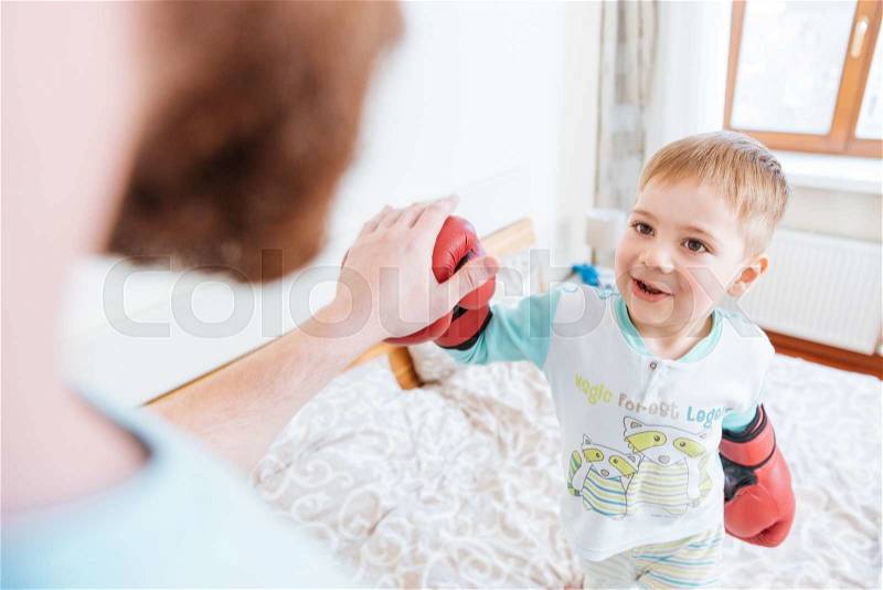 Happy little boy playing with his father using boxing gloves, stock photo