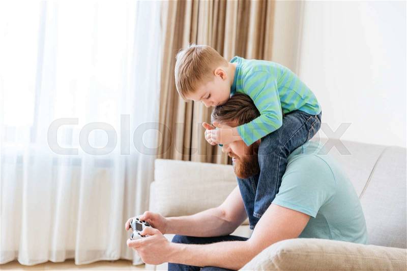 Man sitting on sofa and playing computer games while his little son covering his eyes, stock photo