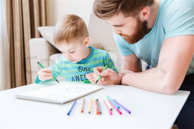 Son and dad sitting and drawing together on the table, stock photo