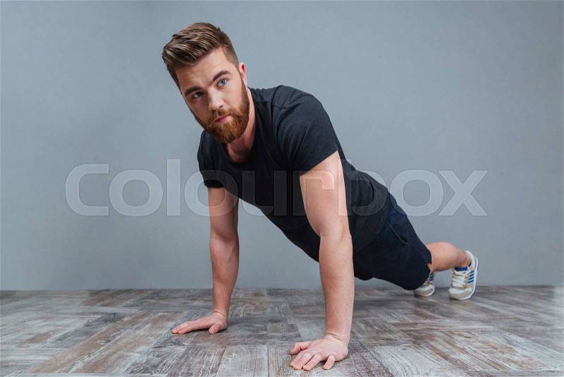 Serious bearded young sportsman doing plank core exercise over grey background, stock photo