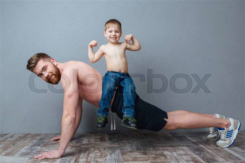 Smiling bearded father doing push-ups with little son sitting on his back , stock photo