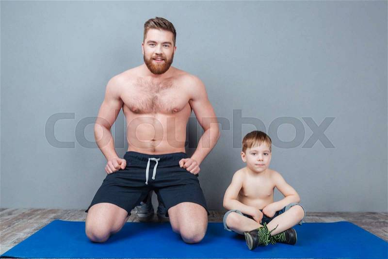 Happy dad and song sitting on blue yoga mat together, stock photo