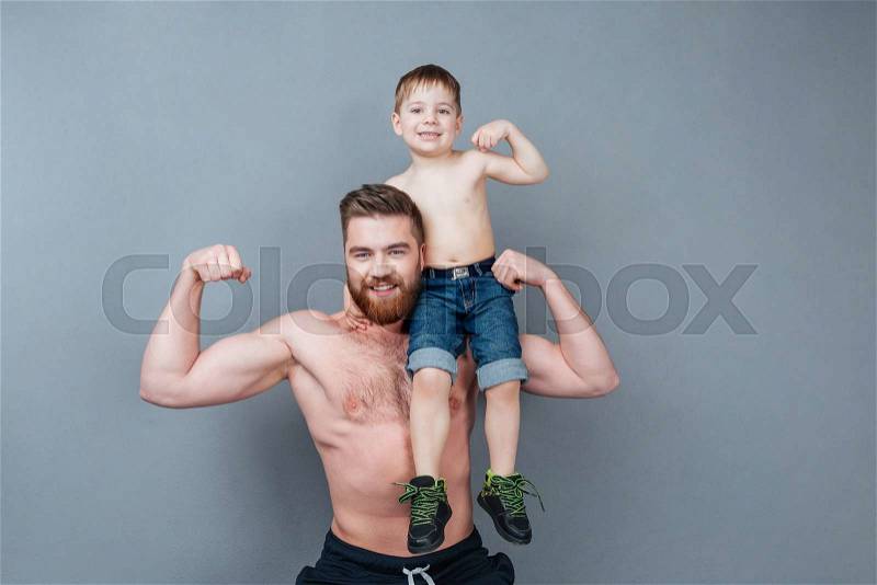 Handsome cheerful strong man holding his little son on his shoulder and showing biceps, stock photo