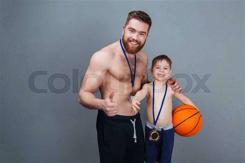 Smiling father and his little son with golden medals holding basketball ball over grey background, stock photo
