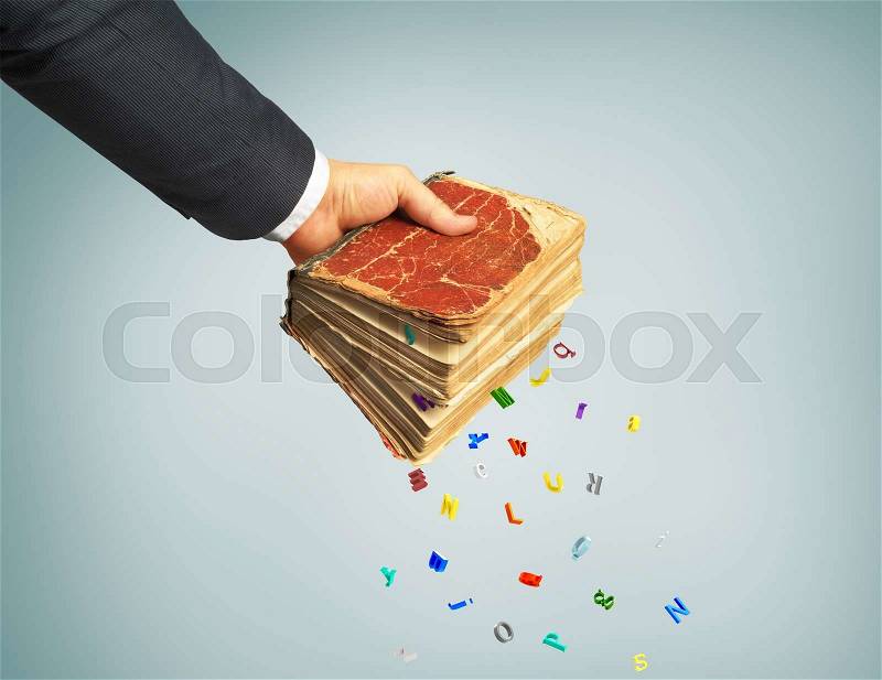 Man\'s hand holding a magic book. From the book letters fallings. Concept of knowledge, stock photo