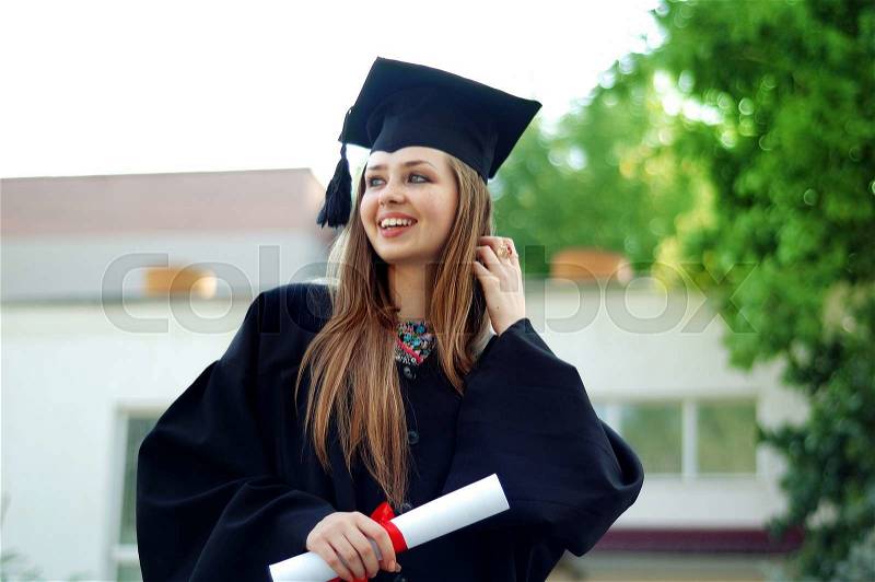 A beautiful graduate girl in the mantle keeps in hands graduate diploma and looks up, stock photo