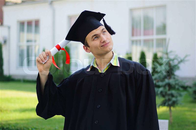 The young man with a diploma in hand and black robe looks at the sky, stock photo