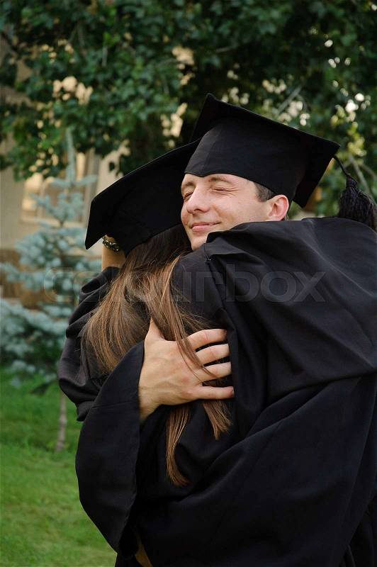 The student in a black gown graduate hugging classmate, stock photo