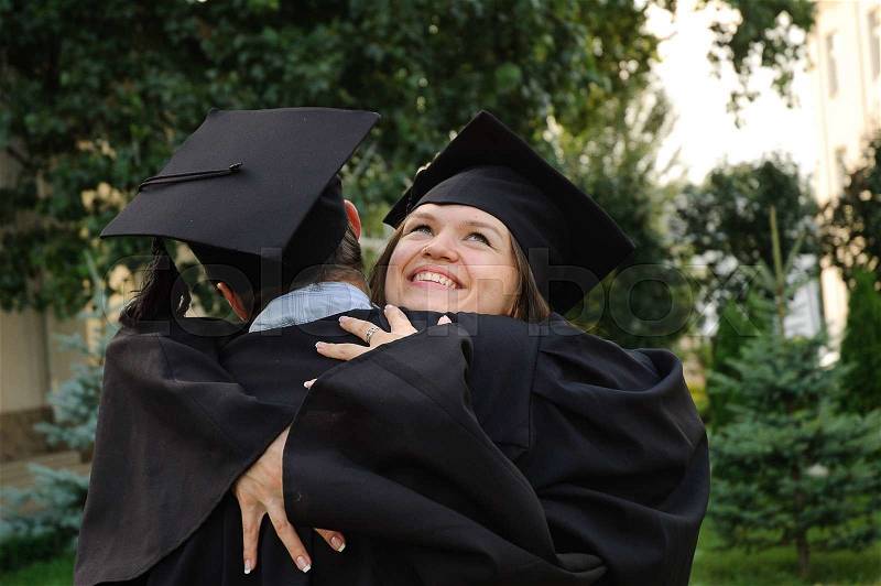 Happy student hugging her boyfriend. The girl looked up. On her face a smile. Both in black robes, stock photo