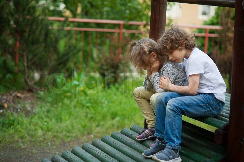 Kids sad sitting together on the bench. The boy hugs a girl. They bowed their heads, stock photo