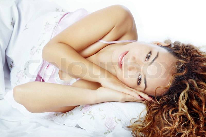Pretty lady with curly hairs laying on a bed, stock photo