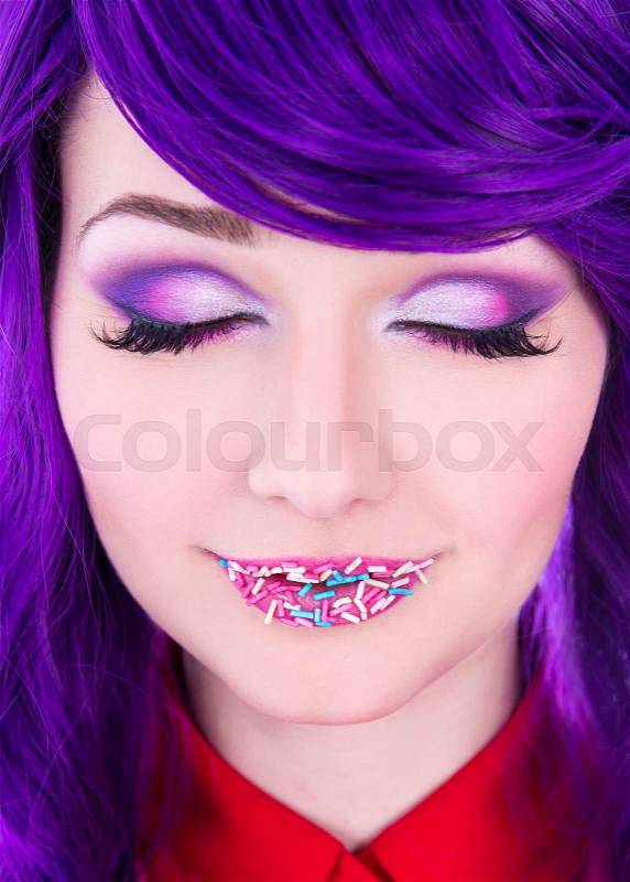Creative makeup - young beautiful woman with purple hair and colorful sugar candies on lips, stock photo