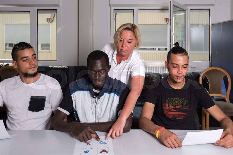Language training for refugees in a German camp: A female German volunteer is teaching young African (Gambia) and Arabic (Algeria and Tunesia) men the German language in a refugee camp quickly errected using accomodation containers. Over 1 million refugee