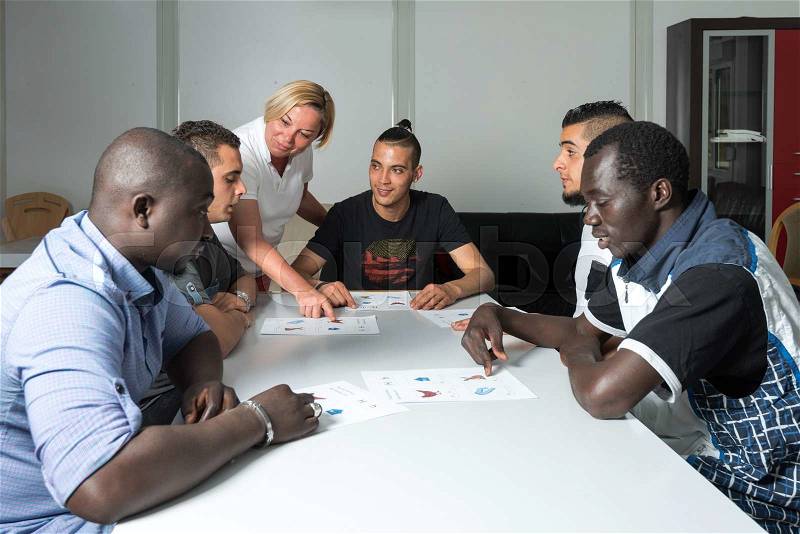 Language training for refugees in a German camp: A female German volunteer is teaching young African (Gambia) and Arabic (Algeria and Tunesia) men the German language in a refugee camp quickly errected using accomodation containers. Over 1 million refugee
