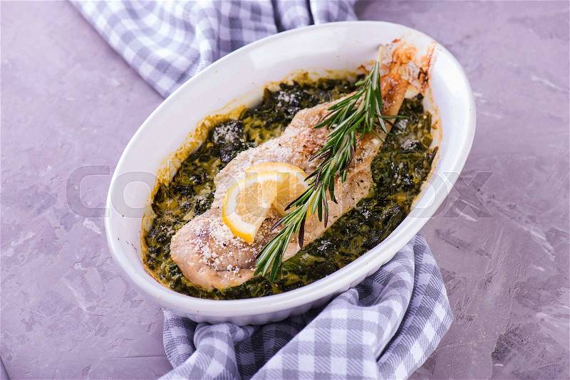 Cooked white fish fillet with herbs on fried spinach in baking dish, stock photo