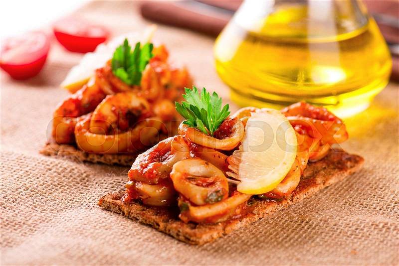 Appetizer with spicy tomato squids and lemon on toast, stock photo