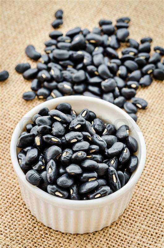 Black bean seeds in white cup on sack background, stock photo