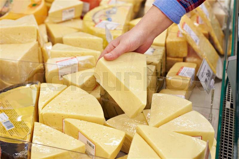 Hand with a piece of cheese in supermarket, stock photo