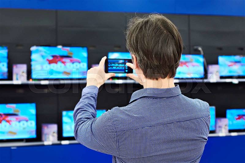 Man shoots with a smartphone TVs in shop, stock photo
