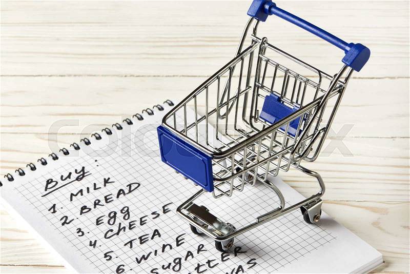 Shopping list and shopping cart on wooden background, stock photo