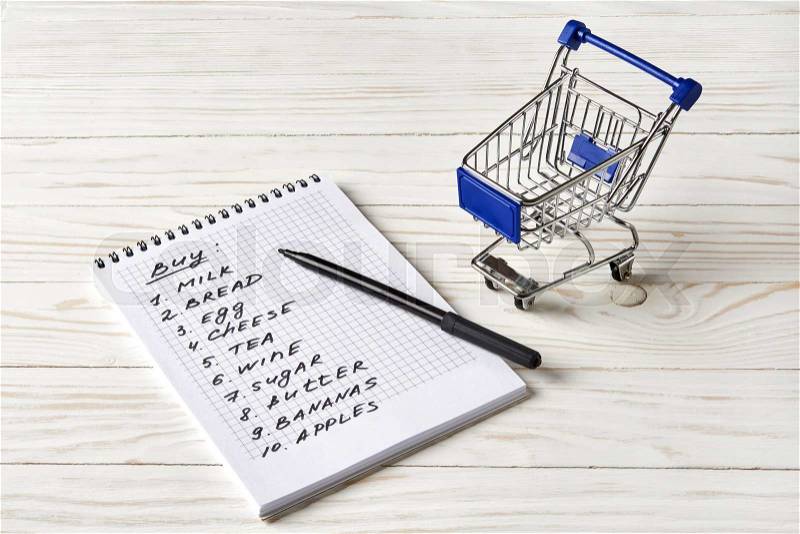 Shopping list and shopping cart on wooden background, stock photo