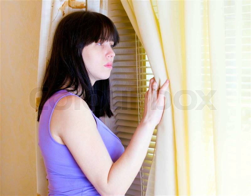 A woman standing at the window and looks out the window, stock photo