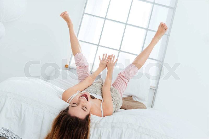 Funny woman lying on the bed with raised legs up at home, stock photo