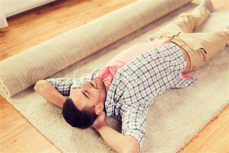 People, repair and renovation concept - happy man lying carpet or rug on floor at home, stock photo