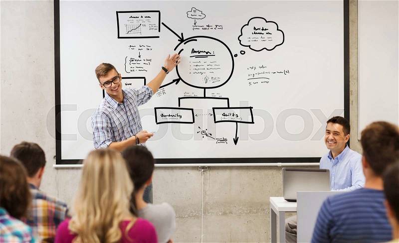 Education, high school, planning and people concept - student standing with remote control in front of teacher and classmates and showing scheme on white board in classroom, stock photo