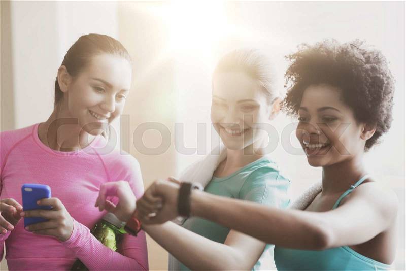 Fitness, sport, training, gym and lifestyle concept - happy women showing time on wrist watch in gym, stock photo