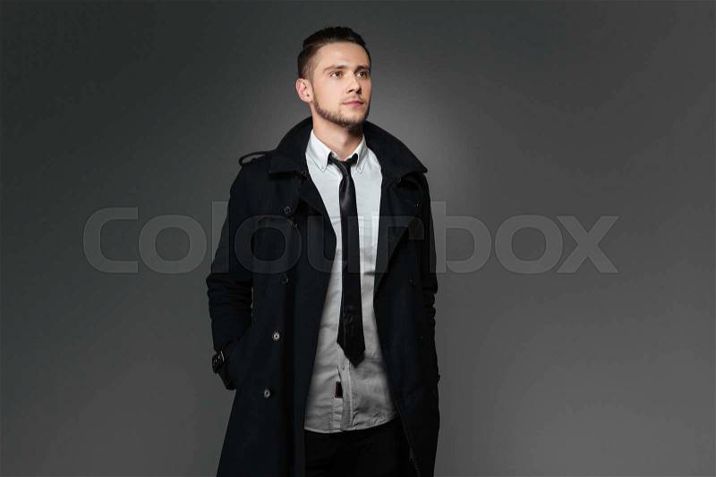 Attractive young businessman in black coat standing with hands in pockets, stock photo