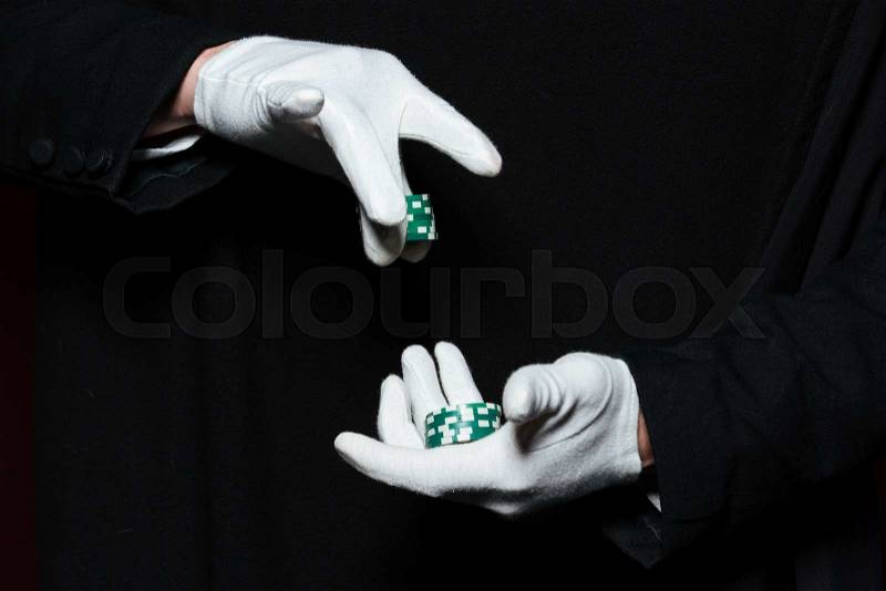 Hands of man magician in white gloves holding green casino chips over black background, stock photo