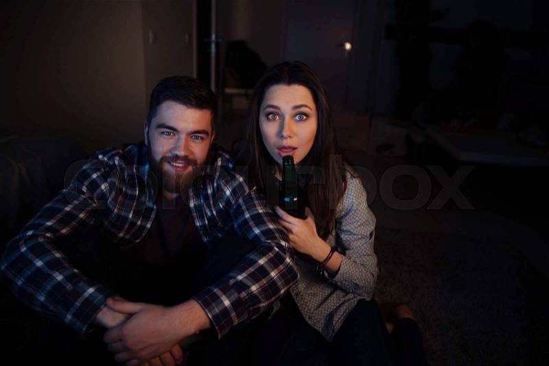 Happy young couple sitting and watching tv in the dark room at home, stock photo
