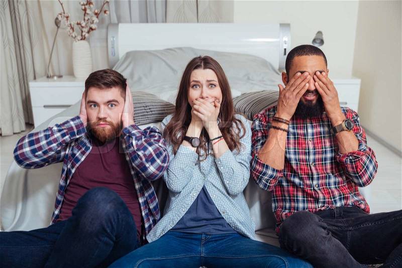 Three young friends sitting in see so evil, hear no evil, speak no evil poses at home, stock photo