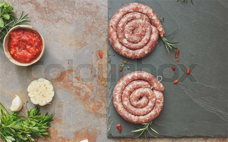 Raw sausages. Raw uncooked gourmet sausages with rosemary with rosemary and spices on a rustic background. Overhead view, vintage toned image, blank space, stock photo