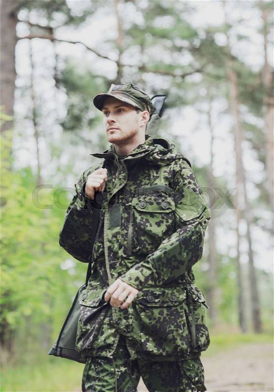 Hunting, war, army and people concept - young soldier, ranger or hunter with gun walking in forest, stock photo