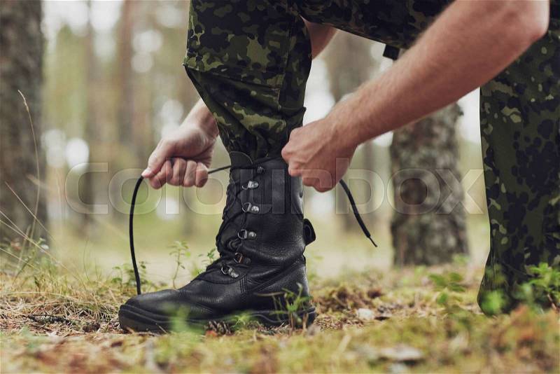 War, hiking, army and people concept - close up of soldier boots and hands tying bootlaces in forest, stock photo